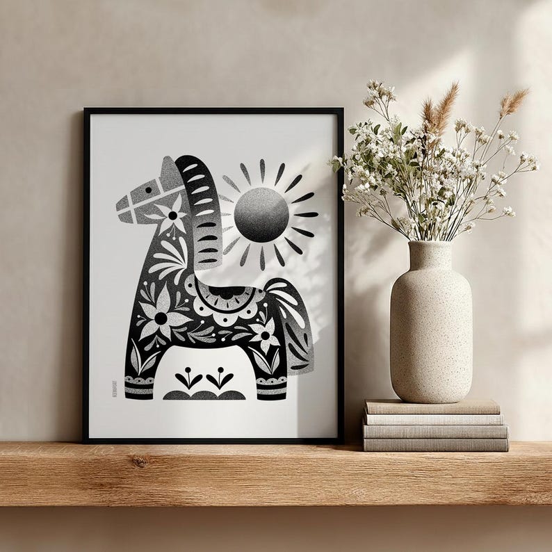 以下が含まれることがあります： 花柄と幾何学模様が施された、様式化された馬が描かれた白黒の額入りアートプリント。馬の後ろには太陽のグラフィックがあります。プリントは、花の入った花瓶と一緒に木製の棚に飾られています。