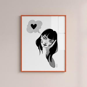 May include: A framed black and white illustration of a woman with black hair and a thought bubble with a heart. The artwork has a minimalist style and is framed in an orange frame.