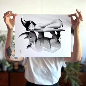 Może przedstawiać: Czarno-biały wydruk artystyczny przedstawiający leżącą postać z rogami na byczej formie. Grafika ma szczeg&oacute;łową, kropkowaną fakturę, tworząc obraz w skali szarości. Wydruk jest trzymany przez osobę.