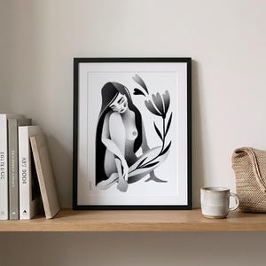 Może przedstawiać: Czarno-biały wydruk artystyczny w czarnej ramie. Grafika przedstawia siedzącą postać z długimi włosami i kwiatem. Wydruk jest eksponowany na drewnianej p&oacute;łce z książkami, kubkiem i plecioną torbą.