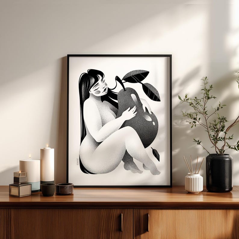 May include: Black and white art print of a seated figure embracing a large pear. The illustration features a woman with long black hair, holding the fruit with leaves. The artwork is framed and displayed on a wooden cabinet.