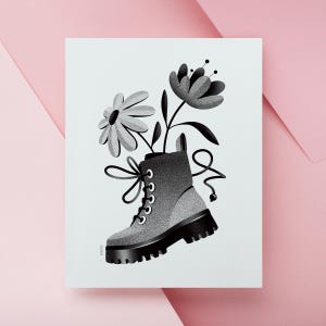 May include: Black and white illustration of a combat boot with flowers growing out of it. The boot is gray with black laces and a thick black sole. Two flowers with black stems and leaves are coming out of the boot. The background is white with a pink border.