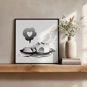 K&ouml;nnte beinhalten: Schwarz-Wei&szlig;-Kunstdruck in einem schwarzen Rahmen. Das Kunstwerk zeigt ein Gesicht, das aus dem Wasser auftaucht, mit einer Gedankenblase mit einem Herz. Eine Vase mit Blumen steht auf einem Holzregal.