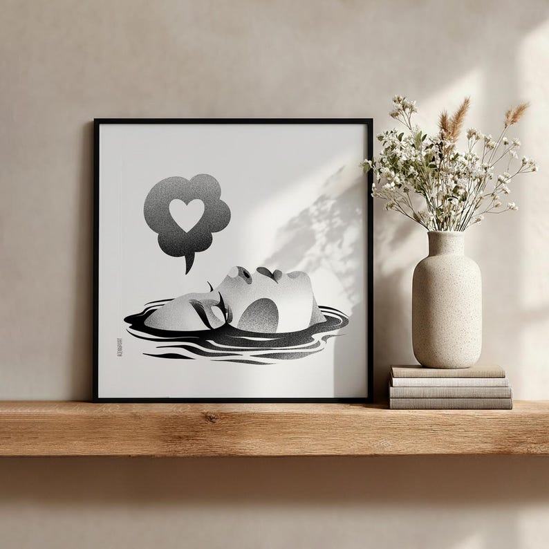 K&ouml;nnte beinhalten: Schwarz-Wei&szlig;-Kunstdruck in einem schwarzen Rahmen. Das Kunstwerk zeigt ein Gesicht, das aus dem Wasser auftaucht, mit einer Gedankenblase mit einem Herz. Eine Vase mit Blumen steht auf einem Holzregal.