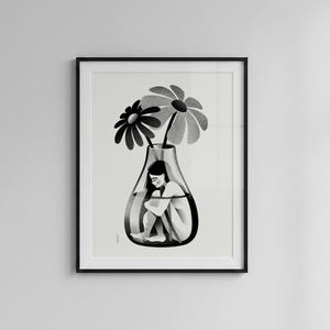 以下が含まれることがあります： 白黒の額入りアートプリント。ガラスの花瓶の中に丸まっている人物と、その上に2つの大きな花が描かれています。イラストはミニマルで、内省的な感覚を伝えています。
