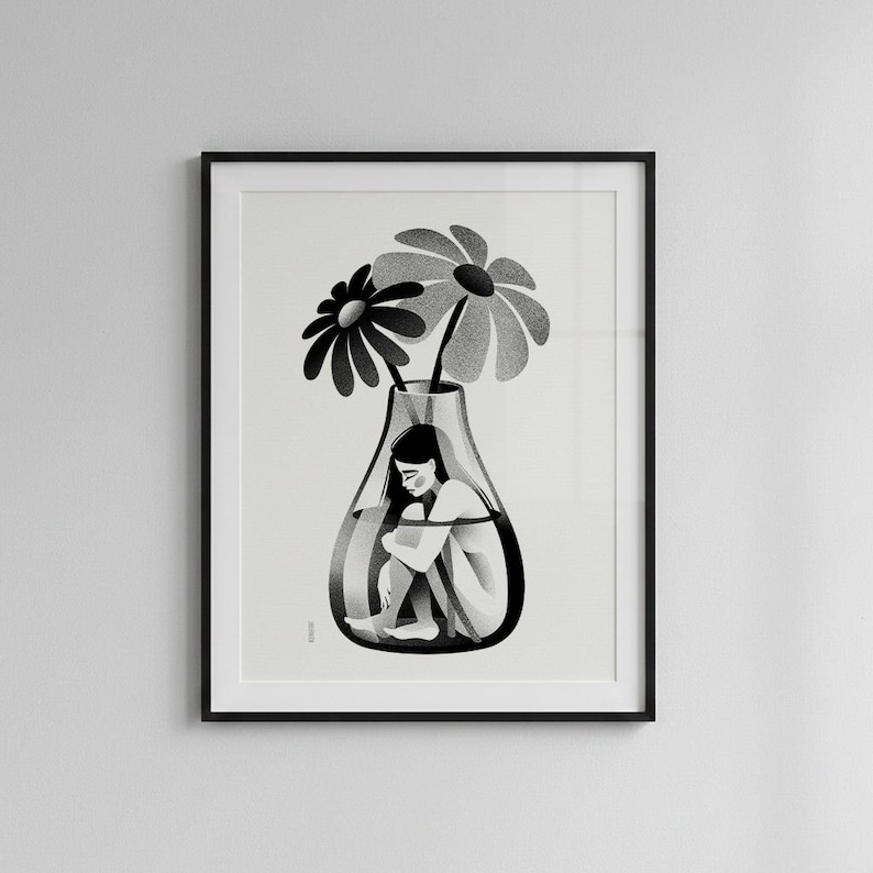 以下が含まれることがあります： 白黒の額入りアートプリント。ガラスの花瓶の中に丸まっている人物と、その上に2つの大きな花が描かれています。イラストはミニマルで、内省的な感覚を伝えています。