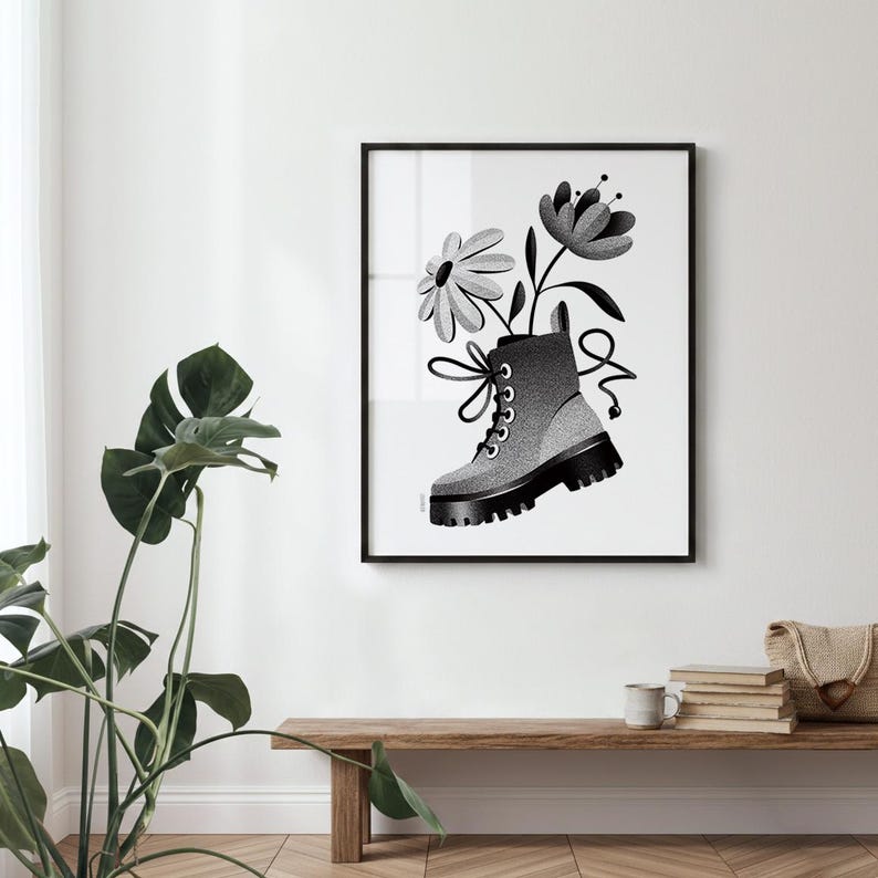 May include: Black and white framed art print featuring a combat boot with flowers. The boot is gray with black accents and laces, and the flowers are stylized. The artwork is displayed on a white wall.