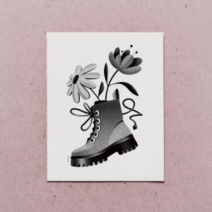 May include: Black and white illustration of a combat boot filled with flowers. The boot has a thick sole, laces, and a loop at the top. Two flowers, one daisy-like and one more structured, emerge from the boot.