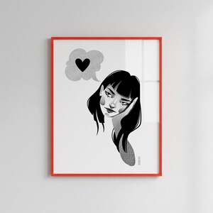May include: A framed art print featuring a black and white illustration of a woman with black hair, resting her head on her hand. A thought bubble with a black heart floats above her head. The frame is red.