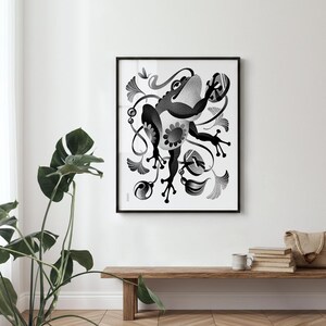 May include: Framed black and white art print. The artwork features a stylized frog illustration with floral and abstract elements. The frog is the central focus, with a whimsical design. The print is in a black frame, suitable for various decor styles.