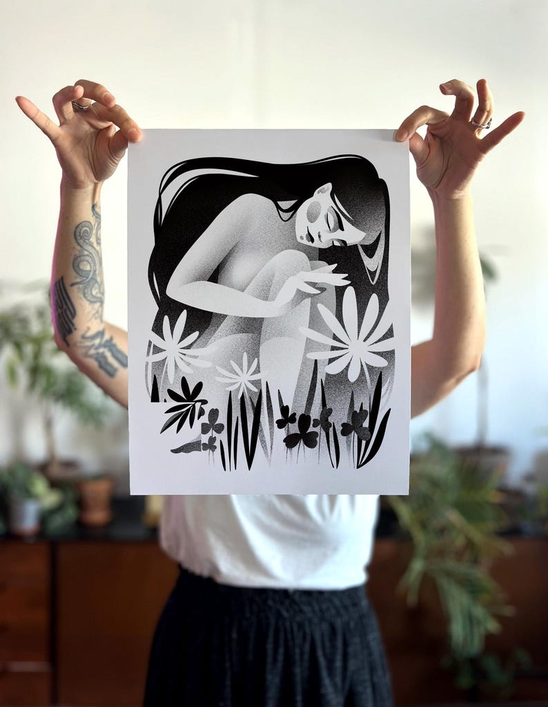 以下が含まれることがあります： 長い髪の座っている人物が、様式化された花と葉に囲まれた白黒のアートプリント。アートワークは柔らかく点描のテクスチャで、夢のような雰囲気を作り出しています。人物は瞑想的なポーズをとっています。