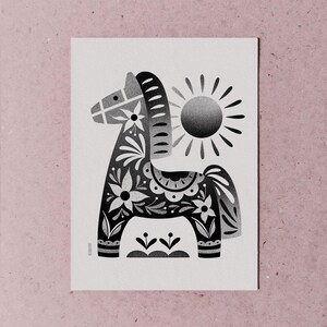 以下が含まれることがあります： 花柄と太陽が描かれた、白黒のダーラナホースのイラスト。馬は花やその他のデザインで装飾されています。太陽は光線で描かれています。アートワークは白い背景にあります。