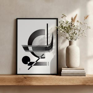 Peut inclure: Impression d'art abstrait encadr&eacute;e en noir, pr&eacute;sentant des formes g&eacute;om&eacute;triques en nuances de gris et de noir. L'&oelig;uvre comprend un demi-cercle, des lignes et un rectangle. Un vase de fleurs blanches et des livres sont sur une &eacute;tag&egrave;re en bois.
