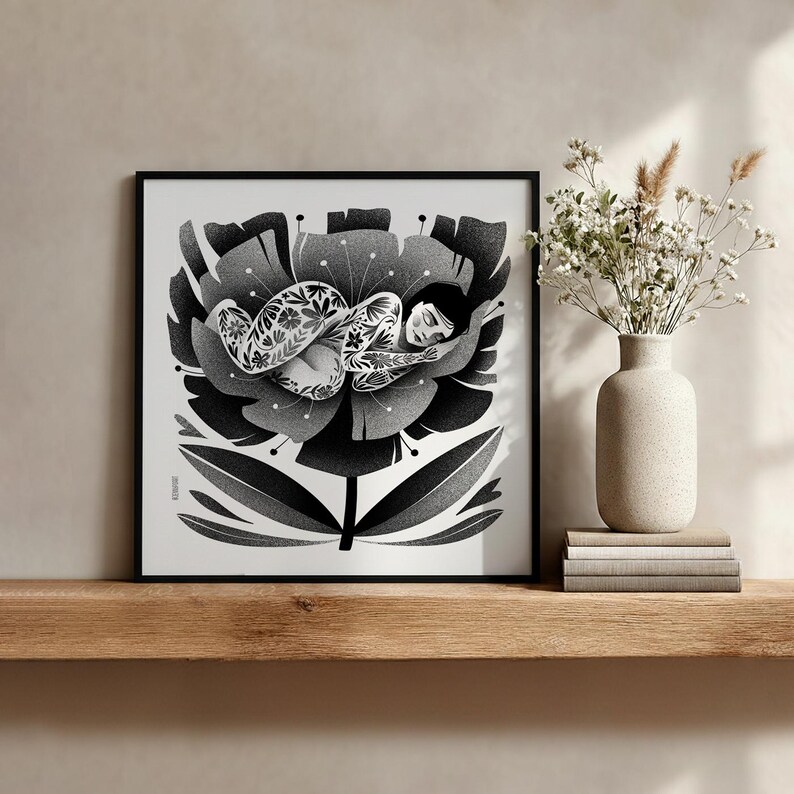 May include: Black and white art print of a person sleeping inside a large flower. The person has floral tattoos. The flower is detailed with dark and light gray shading. The print is in a black frame and sits on a wooden shelf.