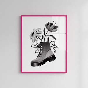 May include: Black and white art print of a combat boot with flowers emerging from the top. The boot is gray with black accents and laces. The artwork is framed in a bright pink frame.