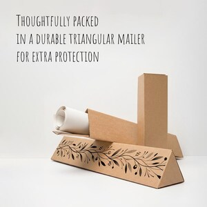 May include: A rolled-up canvas print inside a brown triangular mailer. The mailer has a decorative black and white floral design. Text on the image reads: "THOUGHTFULLY PACKED IN A DURABLE TRIANGULAR MAILER FOR EXTRA PROTECTION."