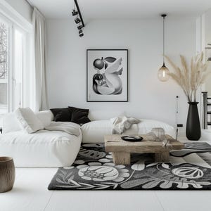 May include: A modern living room with a white sofa, black and white patterned rug, and a wooden coffee table. A framed black and white art print hangs on the wall. A black vase holds tall, dried plants. The room has a minimalist design.