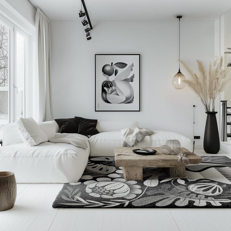 May include: A modern living room with a white sofa, black and white patterned rug, and a wooden coffee table. A framed black and white art print hangs on the wall. A black vase holds tall, dried plants. The room has a minimalist design.