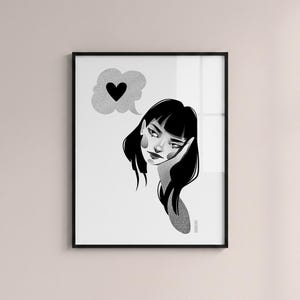 May include: Black and white framed art print featuring a stylized illustration of a woman with black hair, resting her head on her hand. A thought bubble with a black heart floats above her head. The artwork has a minimalist style.