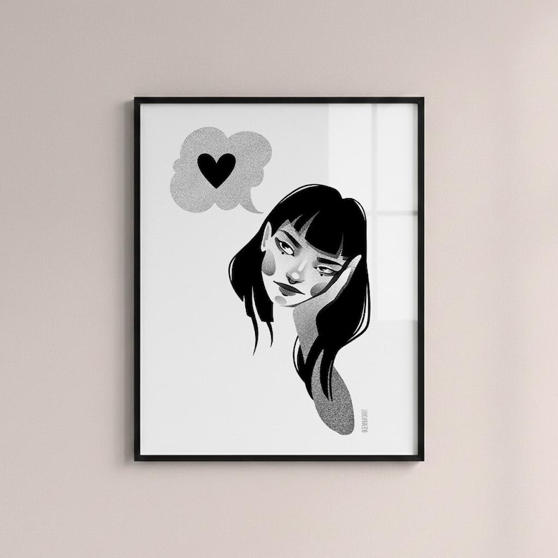 May include: Black and white framed art print featuring a stylized illustration of a woman with black hair, resting her head on her hand. A thought bubble with a black heart floats above her head. The artwork has a minimalist style.