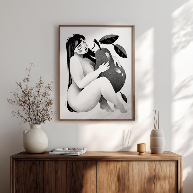 May include: Black and white art print of a seated figure embracing a large pear. The artwork is framed in a wooden frame and hangs on a white wall. The print has a minimalist style and is a modern piece of art.