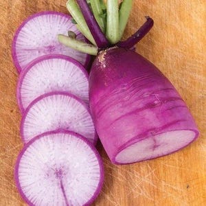 Puede incluir: Un r&aacute;bano daikon morado con tallos verdes, que presenta una pieza grande y cuatro rodajas circulares finas. La piel exterior es de un color morado intenso y vibrante, mientras que la pulpa interior de las rodajas muestra un color blanco p&aacute;lido.
