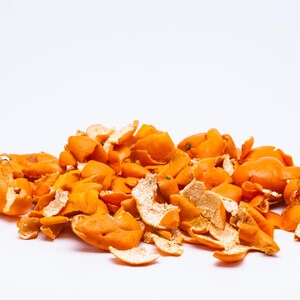 May include: A pile of dried orange citrus peels with a vibrant orange exterior and a pale, textured white interior. The pieces are irregular in shape, curled, and scattered in a loose cluster, showcasing the natural texture of the fruit skin.