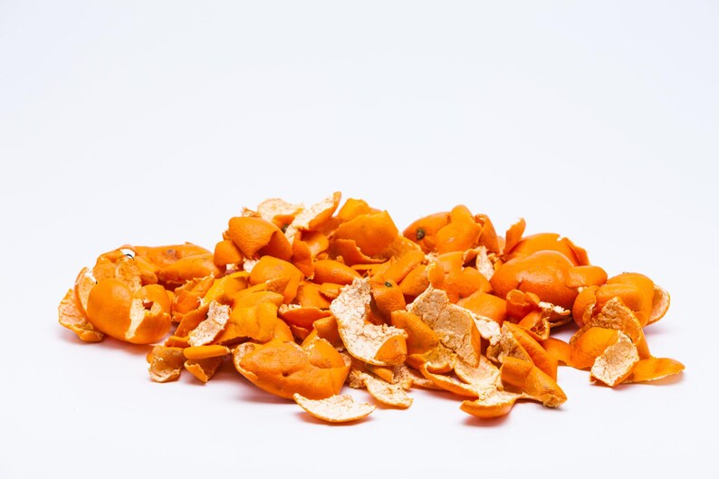 May include: A pile of dried orange citrus peels with a vibrant orange exterior and a pale, textured white interior. The pieces are irregular in shape, curled, and scattered in a loose cluster, showcasing the natural texture of the fruit skin.