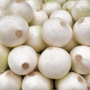 May include: A large collection of fresh white onions piled together. Each onion features a smooth, papery white skin with a light sheen and a small, dried brown root end visible at the centre of the top of each individual round vegetable bulb.