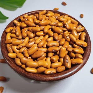 Puede incluir: Un cuenco de madera de color marr&oacute;n oscuro lleno de una gran cantidad de frijoles amarillos secos. Cada frijol tiene una forma ovalada lisa y presenta un peque&ntilde;o ojo o hilio blanco distintivo en el lateral. Varios frijoles sueltos est&aacute;n esparcidos.