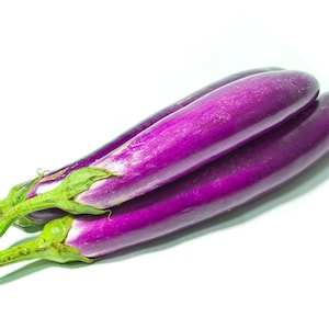 Op de afbeelding: Drie lange, slanke aubergines met een gladde, glanzende, dieppaarse schil en felgroene kelkbladeren aan de steelaanzet. De groenten zijn in een groepje gerangschikt en tonen hun langwerpige, cilindrische vorm en egale paarse kleur.