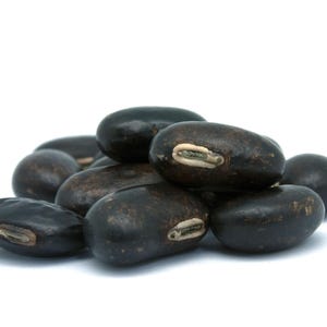 Puede incluir: Un peque&ntilde;o mont&oacute;n de frijoles negros secos, cada uno con un exterior liso, oscuro y de forma ovalada, con una marca de hilio alargada y clara en el lateral. Los frijoles est&aacute;n dispuestos en un grupo, mostrando su color oscuro uniforme.