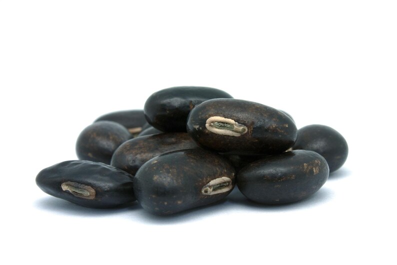 Puede incluir: Un peque&ntilde;o mont&oacute;n de frijoles negros secos, cada uno con un exterior liso, oscuro y de forma ovalada, con una marca de hilio alargada y clara en el lateral. Los frijoles est&aacute;n dispuestos en un grupo, mostrando su color oscuro uniforme.