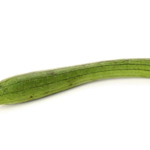 Op de afbeelding: Een lange, slanke luffa-kalebas met een levendige groene schil met duidelijke verticale ribbels die over de hele lengte van de groente lopen. Het oppervlak heeft een licht getextureerd uiterlijk met subtiele kleurvariaties en loopt taps toe naar een afgerond uiteinde.