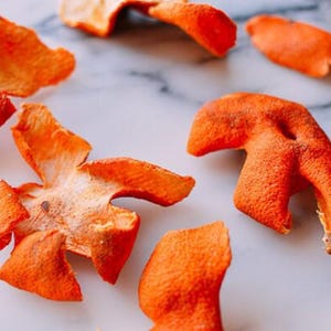 May include: A collection of dried orange citrus peels scattered across the frame. Each piece of peel displays a vibrant, textured orange exterior with a porous surface and a lighter, pale white pith on the underside, showing irregular shapes.