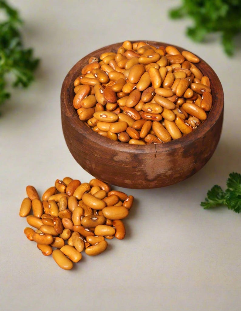 Puede incluir: Un cuenco de madera marr&oacute;n oscuro lleno de numerosos frijoles de color marr&oacute;n claro, con un peque&ntilde;o mont&oacute;n de los mismos frijoles descansando fuera del cuenco. Los frijoles son de forma ovalada con una textura suave y una marca blanca.