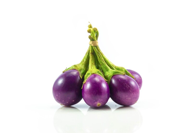May include: A cluster of four small, round, deep purple aubergines with smooth, glossy skin. Each aubergine features a vibrant green calyx and stem, and they are bundled together at the top with a thin, light-coloured rubber band.