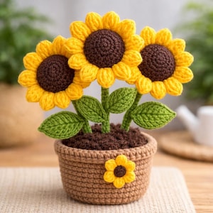 Può includere: Un'arrangiamento di girasoli all'uncinetto in un vaso marrone. I girasoli hanno petali gialli e centri marroni, con foglie e steli verdi. Il vaso è decorato con un piccolo fiore giallo. Un affascinante oggetto decorativo fatto a mano.