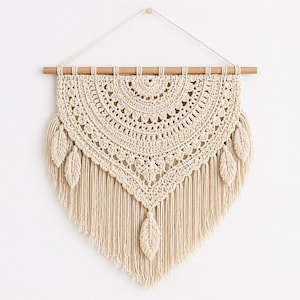 May include: Cream-colored macrame wall hanging with a wooden dowel. The handmade piece features a detailed, semi-circular crochet design with fringe and leaf accents. A decorative, bohemian-style wall art piece.