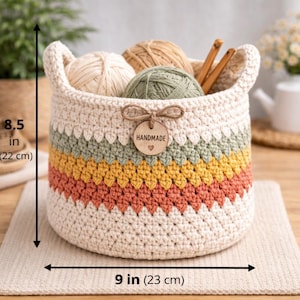 May include: A handmade crochet basket, 8.5 inches (22 cm) tall and 9 inches (23 cm) wide, with a cream-colored base and colorful stripes of green, yellow, and orange. The basket contains yarn balls and crochet hooks. A wooden tag reads "HANDMADE".