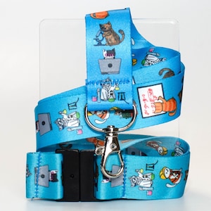 May include: A blue lanyard with a white background and a repeating pattern of cats working on laptops. The lanyard has a black clip and a silver swivel hook. The text "0: 5-6 hrs" is printed on the lanyard.