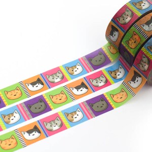 May include: A roll of colorful washi tape with a repeating pattern of cartoon cats in squares. The tape is on a white background and is partially unrolled, showing the design.