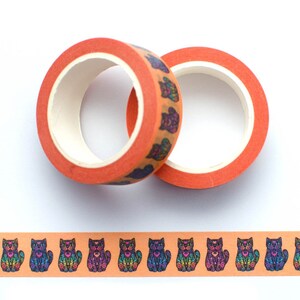 May include: Two rolls of orange washi tape with a repeating pattern of colorful, detailed sugar skull cats. The tape is unrolled to show the pattern.