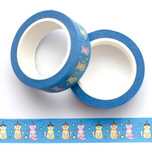 May include: Two rolls of blue washi tape with a pattern of colorful cats wearing unicorn horns. The tape is on a white background.