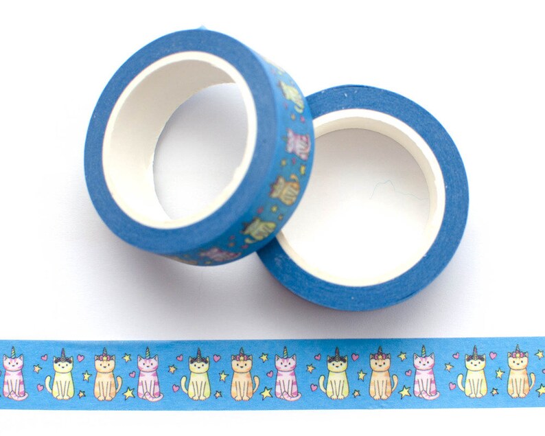 May include: Two rolls of blue washi tape with a pattern of colorful cats wearing unicorn horns. The tape is on a white background.