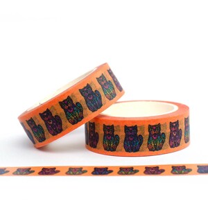 May include: Two rolls of orange washi tape with a repeating pattern of black cats with colorful details. The tape is unrolled on a white surface.