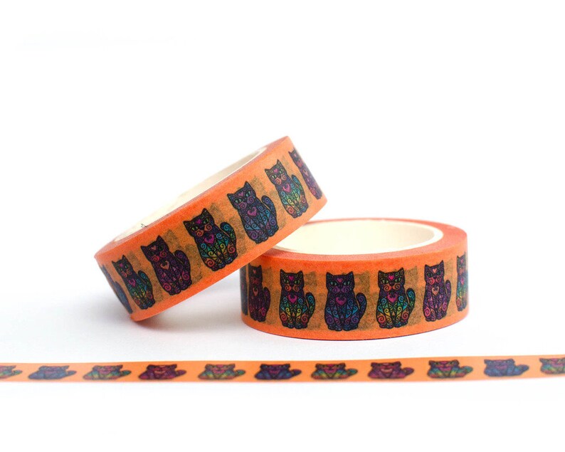 May include: Two rolls of orange washi tape with a repeating pattern of black cats with colorful details. The tape is unrolled on a white surface.