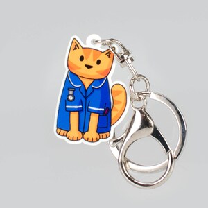 May include: A blue and orange cat wearing a blue nurse's uniform with a stethoscope and a watch. The cat is attached to a silver key chain.