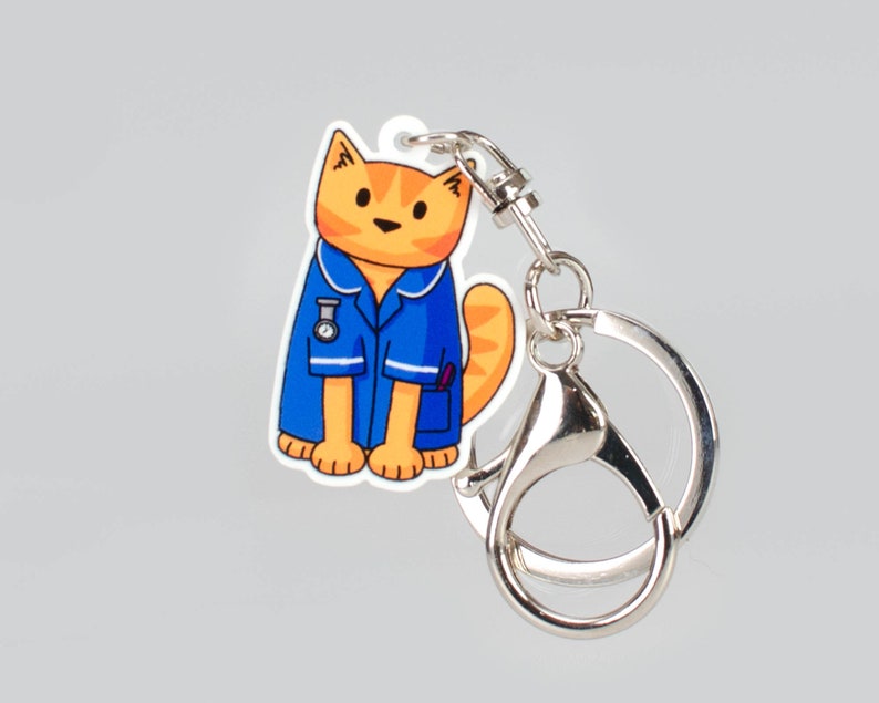 May include: A blue and orange cat wearing a blue nurse's uniform with a stethoscope and a watch. The cat is attached to a silver key chain.