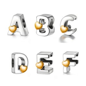Könnte beinhalten: Silberne Buchstaben-Charms mit goldenen Herz-Akzenten. Die Buchstaben A, B, C, D, E und F sind abgebildet. Diese Charms sind für Armbänder oder Halsketten gedacht und bieten eine individuelle Note für Schmuck.